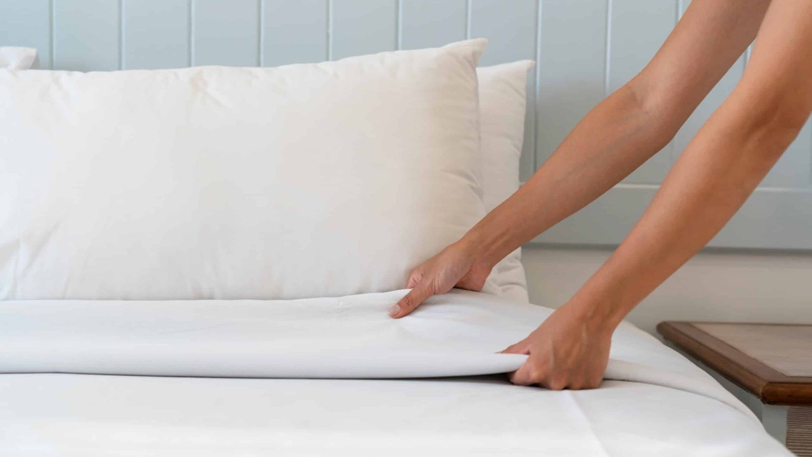 Close up woman hand set up white bed sheet in hotel room, copy space for text.